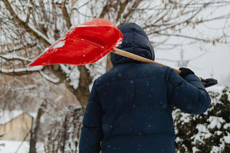 man with red snow shovel over shoulder