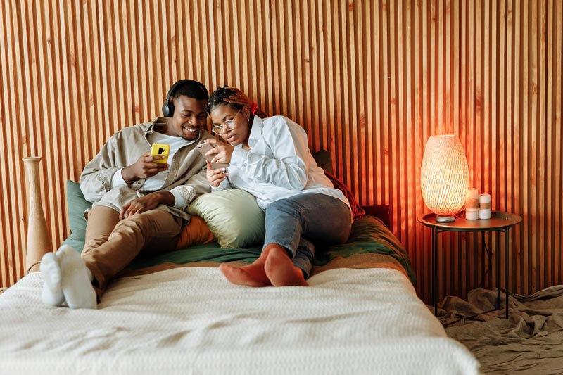 couple lying in bed looking at smartphone