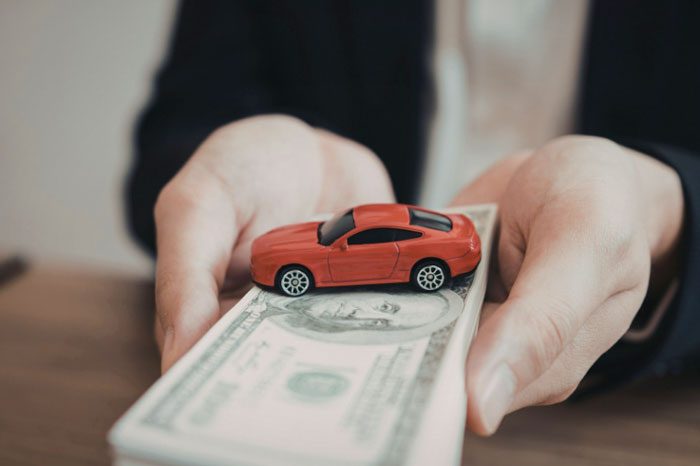 persona holding a stack of hundred dollar bills and toy car