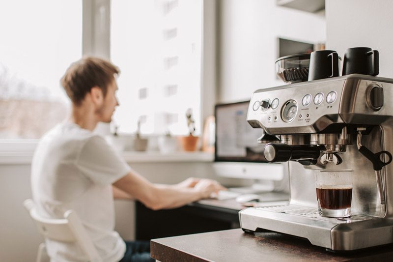 man working at desk with coffee maker in the foregound